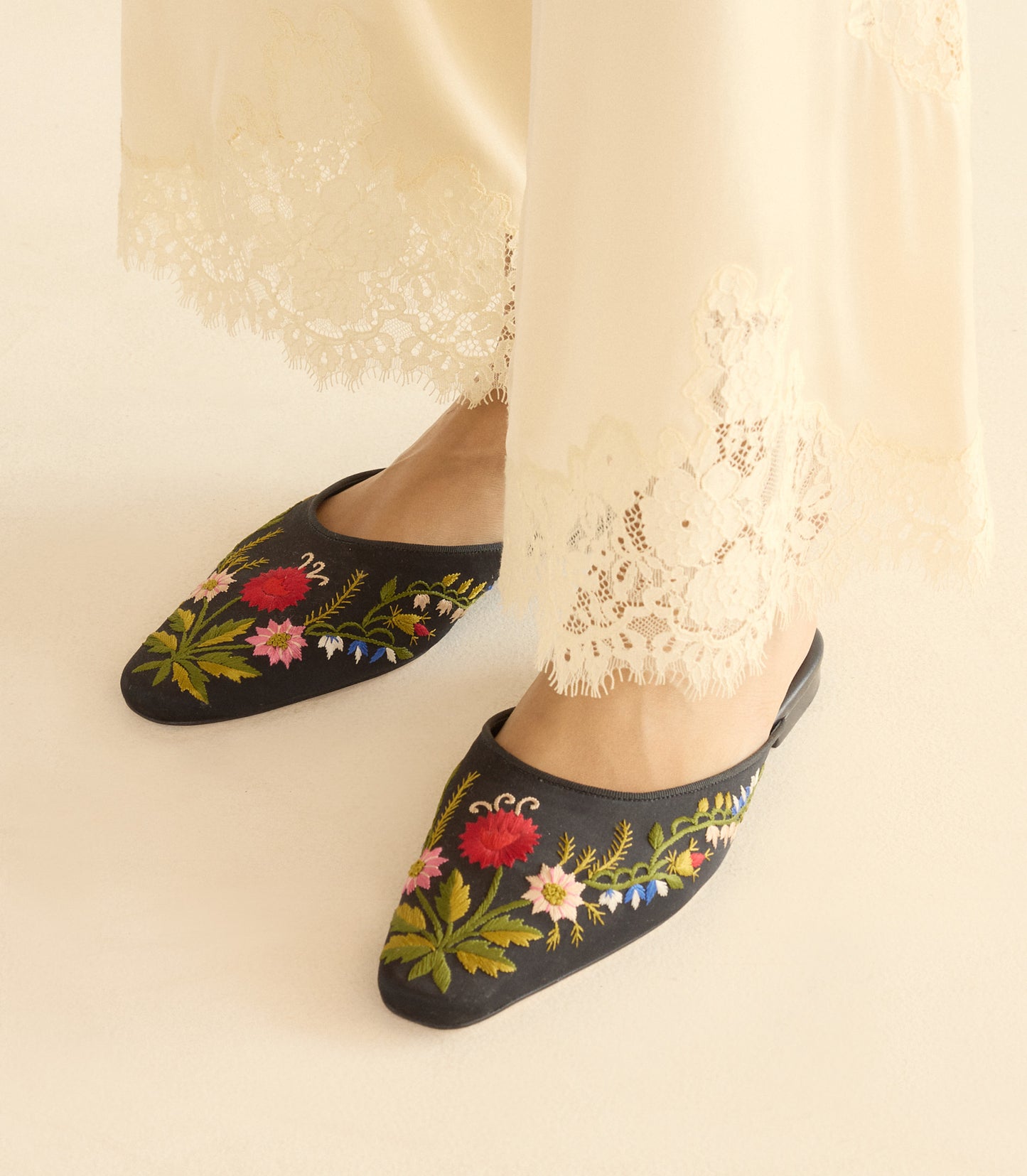Black embroidered slippers with floral designs worn with white pants.