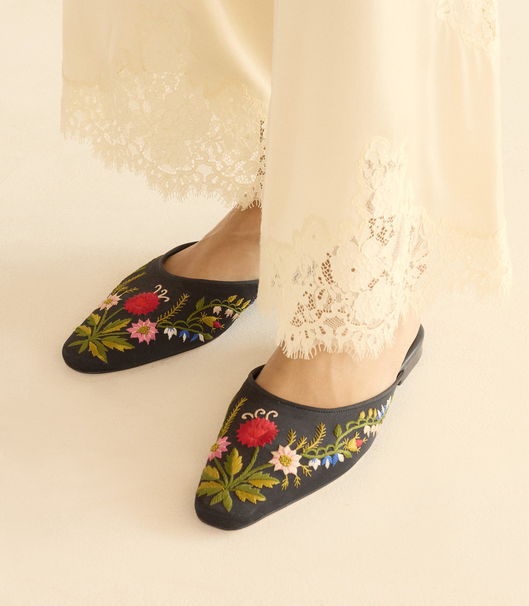 Black embroidered slippers with floral designs worn with white pants. 1