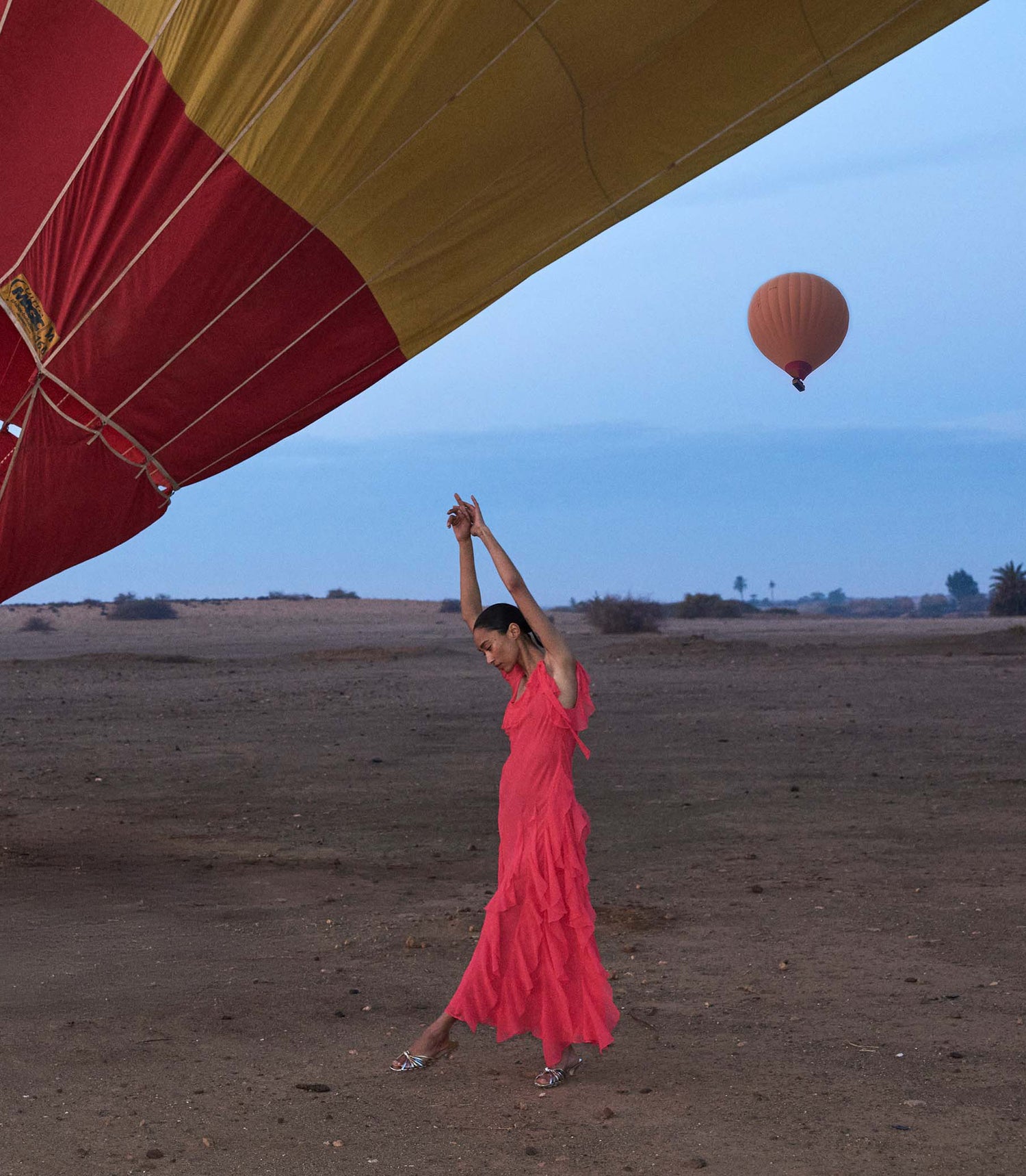 Woman in a pink dress standing on a desert with a hot air balloon in the background